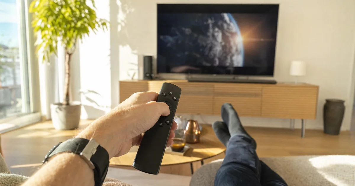 Hand mit Fernbedienung startet einen Film auf dem Fernseher im sonnigen Wohnzimmer